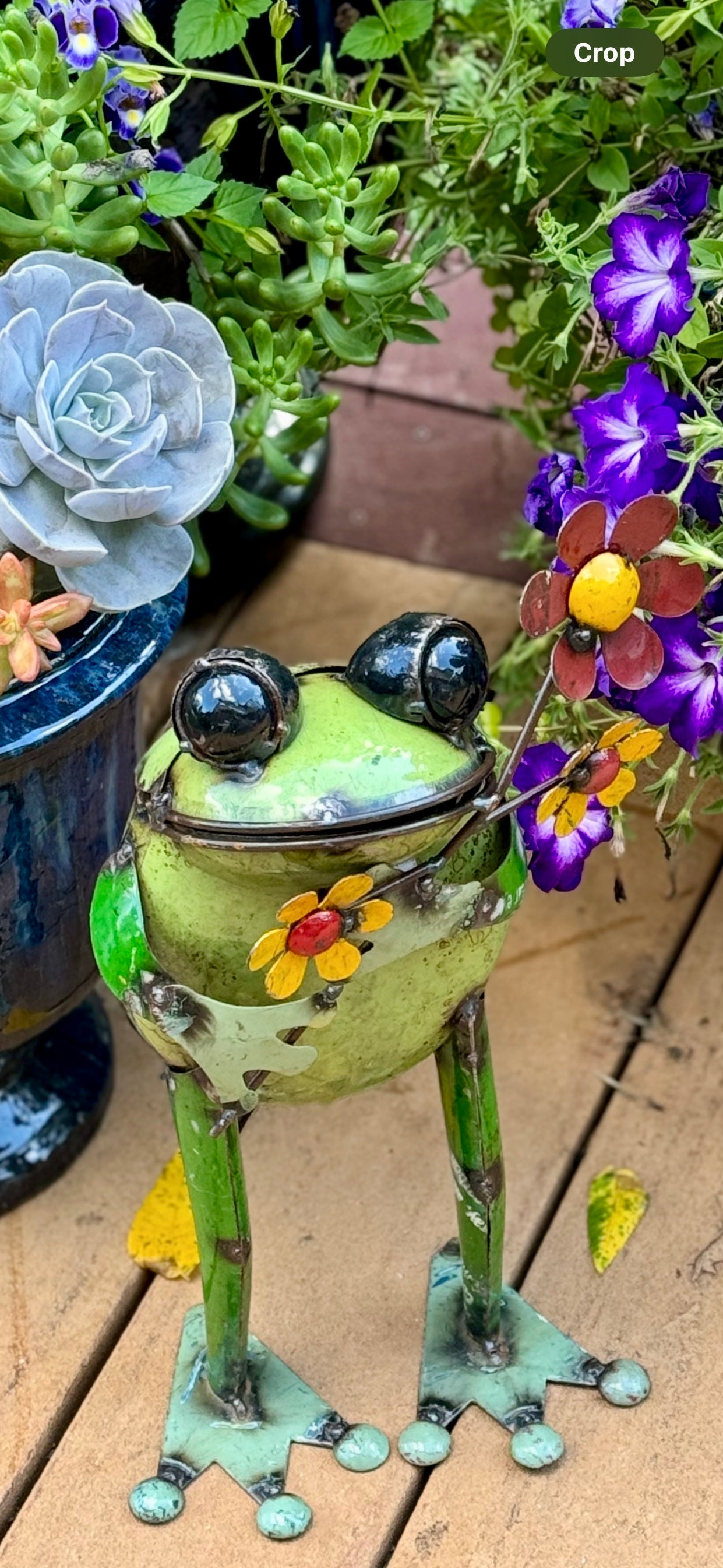 Meet Skip, a reclaimed metal frog made from all recycled materials. Skip is holding a colorful bouquet of red and yellow flowers.